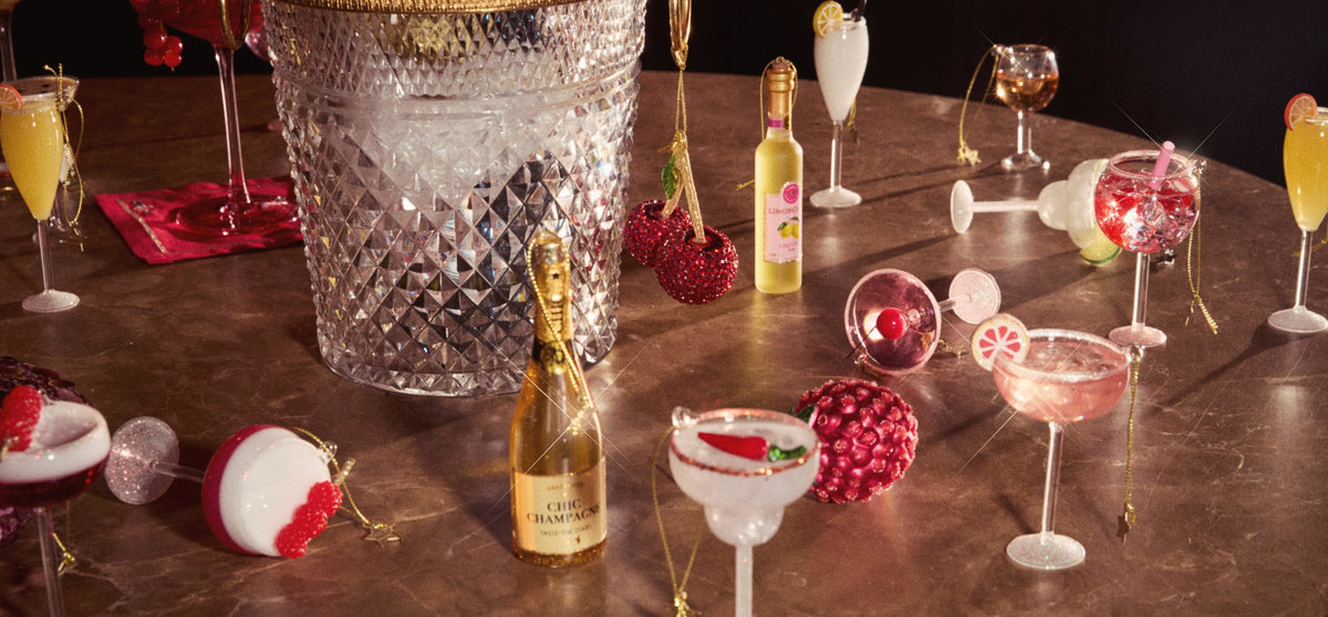 Vondels hand-painted glass cocktail ornaments — champagne, spritz and margarita — around a crystal ice bucket on a marble bar table